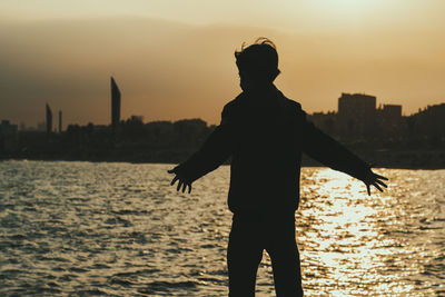 Silhouette man standing by building against sky during sunset