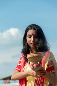 Portrait of a beautiful young woman holding umbrella against sky