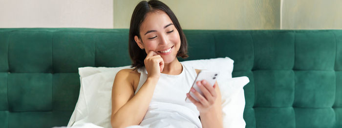 Young woman using phone while sitting on sofa at home