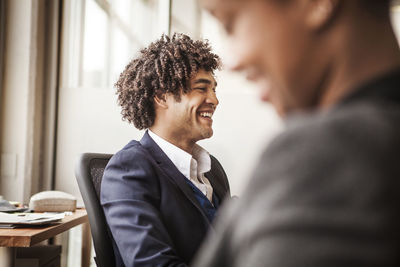 Happy businessman sitting on chair by coworker at office