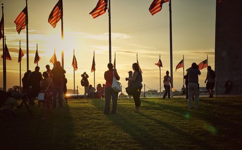 People and american flags on field at washington monument during sunset