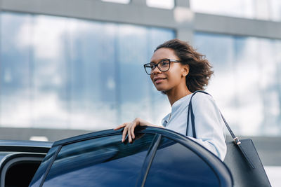 Smiling young woman looking away while standing by car