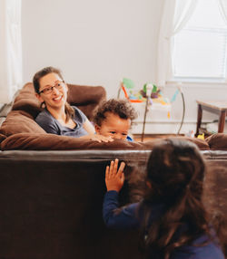 Smiling mother with kids sitting on sofa at home