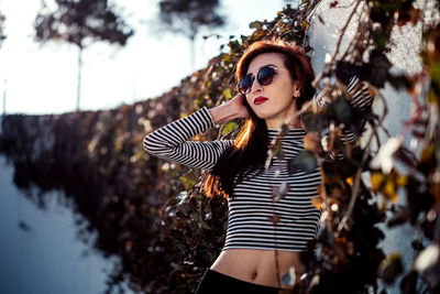 Fashionable woman wearing sunglasses while standing by wall