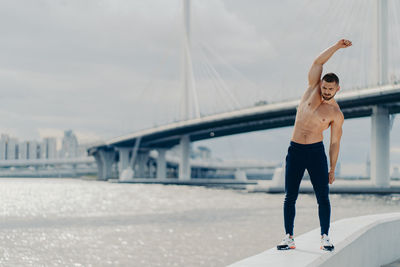 Full length of man exercising on bridge against sky