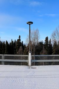 Railing by snow covered trees against blue sky