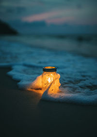 Close-up of illuminated light on beach against sky during sunset