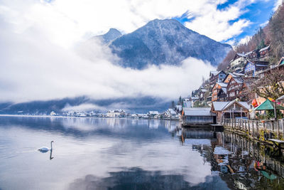 Houses by lake with mountains in background against cloudy sky