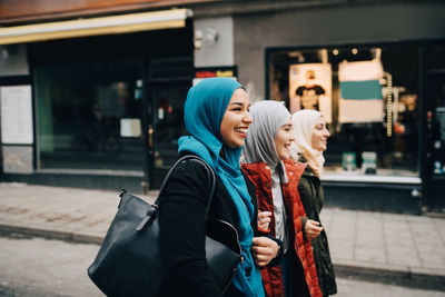 Cheerful young female friends walking with arms in arms on street in city