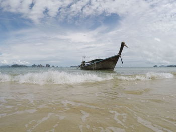 Boat anchored at beach against cloudy sky