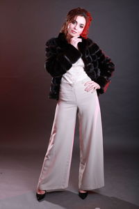 Fashionable young woman wearing fur jacket while standing against gray background