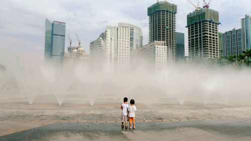 Rear view of people standing by modern cityscape against sky