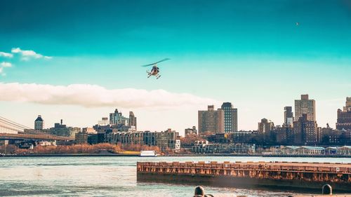 Helicopter flying over river in city against sky