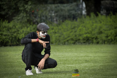 Full length of teenager boy with face paint crouching on grass at park