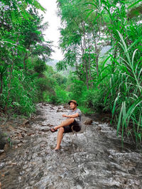 Portrait of young woman sitting on rock by lake