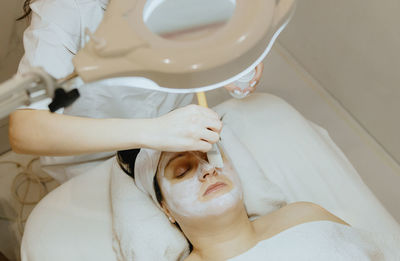 A girl cosmetologist applies a cream mask with a brush to a woman s face.