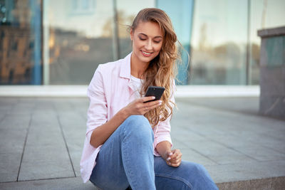 Full length of teenage girl sitting on mobile phone