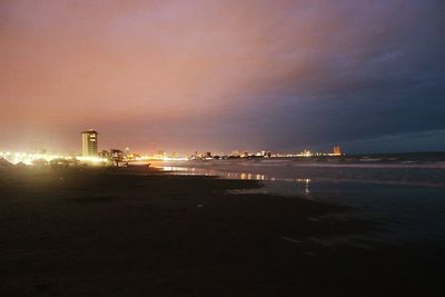 Illuminated buildings by sea against sky at night
