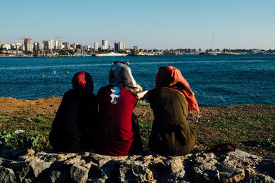 Rear view of friends on sea by cityscape against clear sky