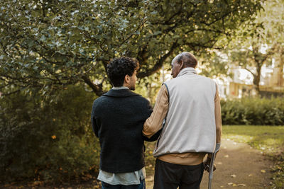 Rear view of male nurse walking with senior male at park