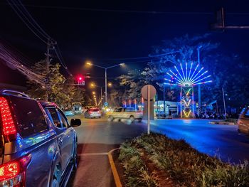 Illuminated road by city against sky at night