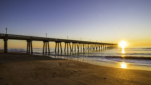 Pier over sea against clear sky during sunset