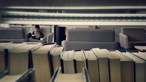 Boy sitting on couch seen through books at shelf