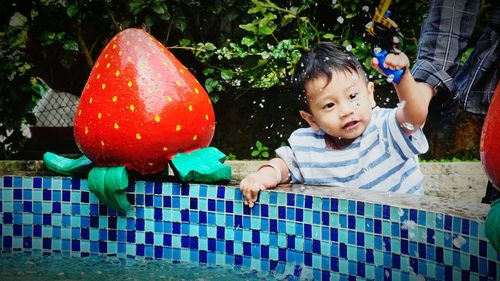 Smiling boy playing with toy gun near fountain at park