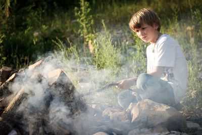 Boy looking at bonfire emitting smoke at campsite