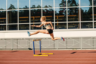 Woman athlete runnner running hurdles in summer athletics competition