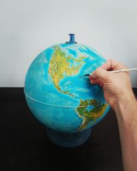 Cropped hand of man marking on globe at table