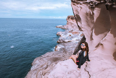 Woman wearing sunglasses sitting on rock formation by sea