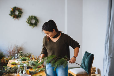 Young woman holding plant decorations at home during christmas