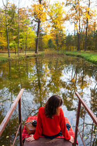 A young woman sits with her back on a bridge near a lake on a sunny day. beautiful autumn