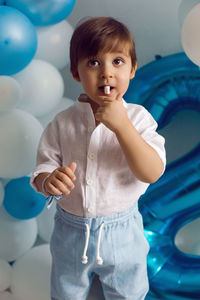 Baby boy in blue pants and shirt standing on the floor in blue and white balloons