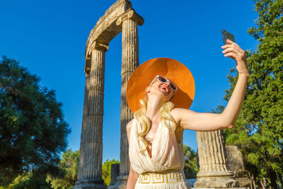 Low angle view of mature woman taking selfie through phone against sky