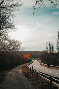 Road by bare trees against sky