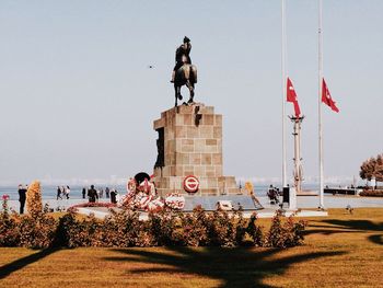 Statue by people in city against sky