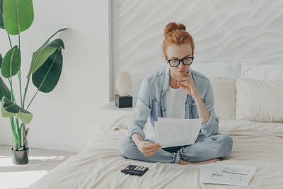 Young woman reading document while sitting on sofa