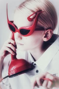 Close-up of retro style girl wearing sunglasses while holding phone against gray background