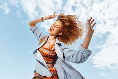 Young woman with arms raised standing against sky