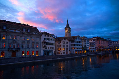 Buildings in city by river at dusk