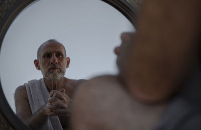 Shirtless adult man looking at himself in mirror