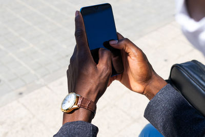 Unrecognizable black male entrepreneur browsing cellphone and reading messages while working in city during sunny day