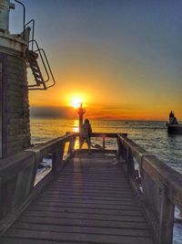 Man standing on pier over sea against sky during sunset