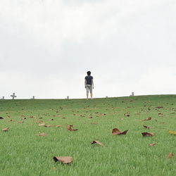 Rear view of man standing by cemeteries on hill against clear sky