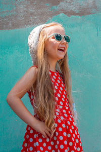 Beautiful happy girl in red polka dot dress smiling turquoise concrete wall background. cute  child 