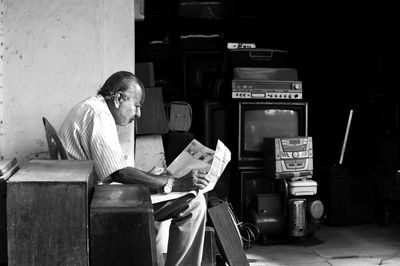 Man reading newspaper while sitting outside shop