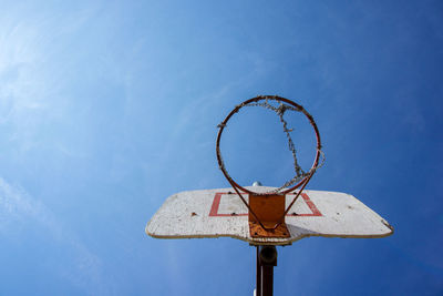 Looking up at outdoors basketball hoop with wooden backboard and blue sunny sky in the background. 