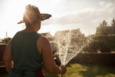 Back view of mature woman gardener watering her garden with hose